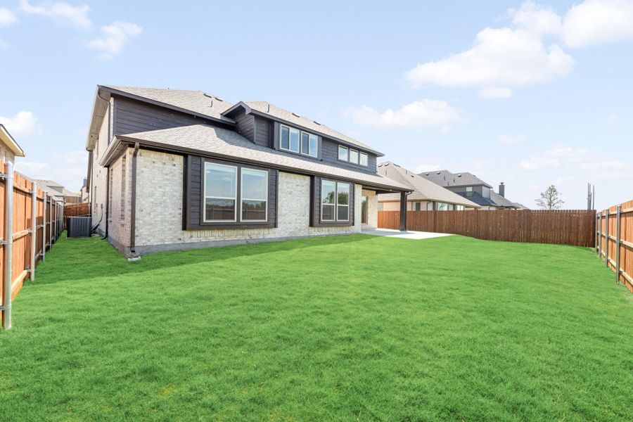 Two-story home with brick and dark siding, large fenced backyard with green lawn and small patio