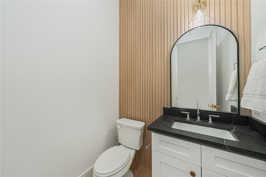 This bathroom features a vanity with a dark countertop and white cabinetry, complemented by a large arched mirror