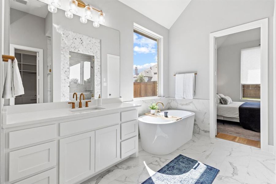 Ensuite bathroom with a wainscoted wall, vanity, a soaking tub, lofted ceiling, and tile walls