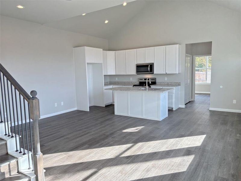 Kitchen with high vaulted ceiling, white cabinets, appliances with stainless steel finishes, a kitchen island with sink, and dark wood finished floors