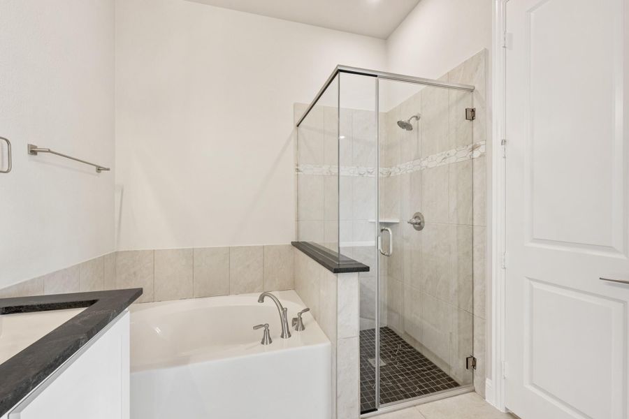 Bathroom with soaking tub, glass-enclosed shower, tile walls, and dark granite countertop Bathroom with soaking tub, glass-enclosed shower, tile walls, and dark granite countertop