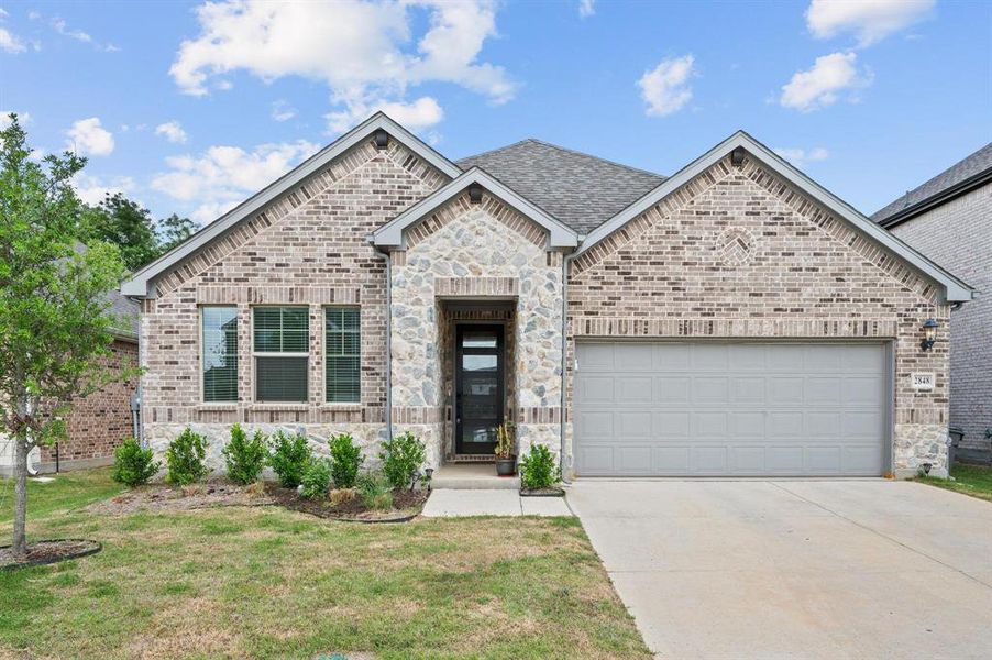 Brick and stone facade featuring an attached garage, covered entry, and established landscaping Brick and stone facade featuring an attached garage, covered entry, and established landscaping