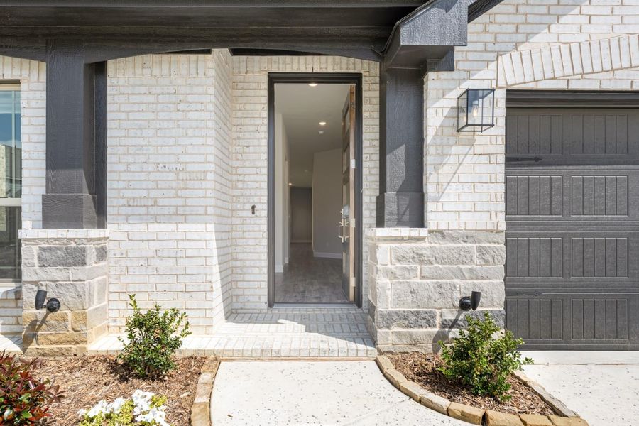 Home entrance with open dark-framed door, white brick exterior, stone accents, and concrete walkway