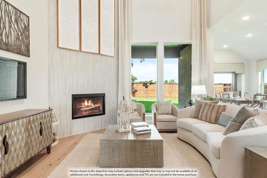 Living room with two-story ceiling, tile fireplace, neutral sofa, and large windows overlooking backyard