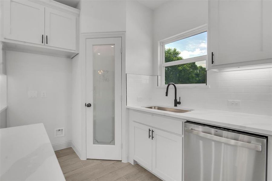 Kitchen with dishwasher, tasteful backsplash, light countertops, white cabinetry, and light wood-type flooring Kitchen with dishwasher, tasteful backsplash, light countertops, white cabinetry, and light wood-type flooring