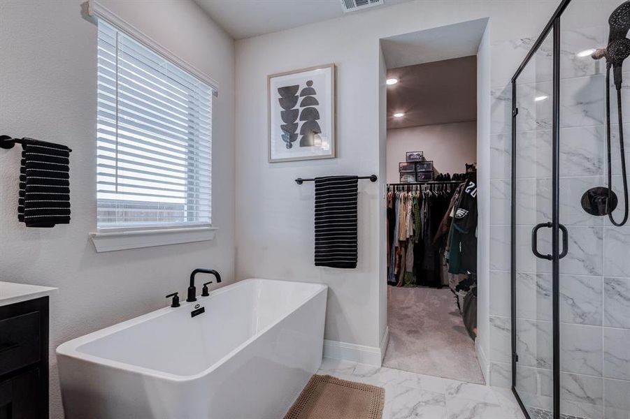 Bathroom with a spacious closet, light marble finish flooring, a freestanding bath, a shower stall, and vanity