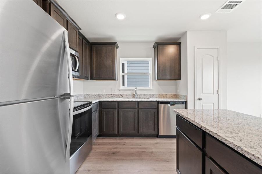 Kitchen featuring light stone counters, dark brown cabinetry, stainless steel appliances, sink, and light hardwood / wood-style flooring