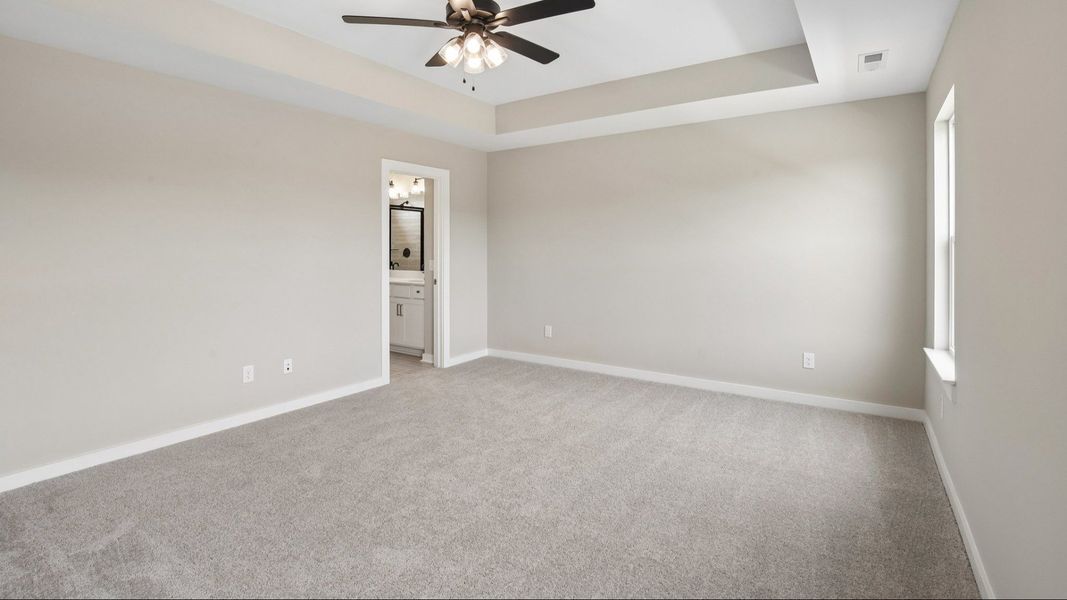 Bedroom with tray ceiling, windows, ceiling fan, and entrance to primary bathroom