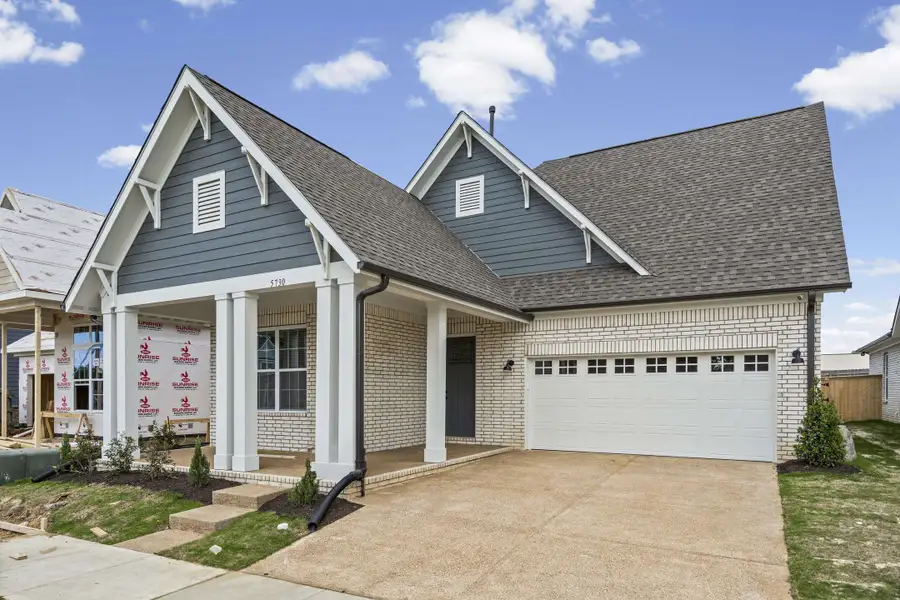 Modern farmhouse-style home featuring a covered front porch, white brick facade, dark gray siding, and a two-car garage with transom windows Modern farmhouse-style home featuring a covered front porch, white brick facade, dark gray siding, and a two-car garage with transom windows