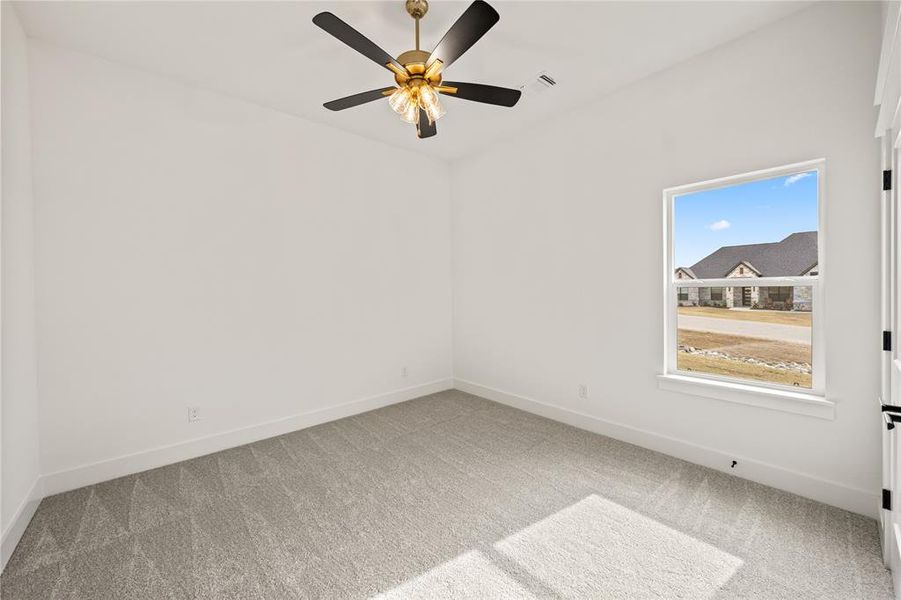 Bright room featuring light grey carpeting, white baseboards, a single window with white trim, and a ceiling fan with black blades and a brass-finish light fixture