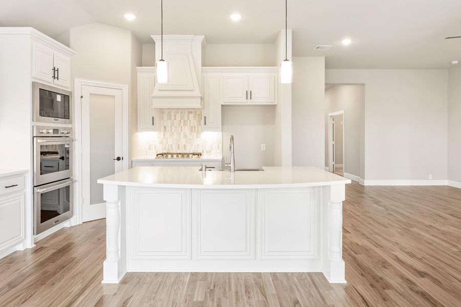 White kitchen with large center island, double wall ovens, pendant lights, and wood floors White kitchen with large center island, double wall ovens, pendant lights, and wood floors