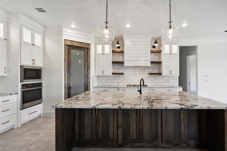 Kitchen with black microwave, tasteful backsplash, hanging light fixtures, oven, and a large island