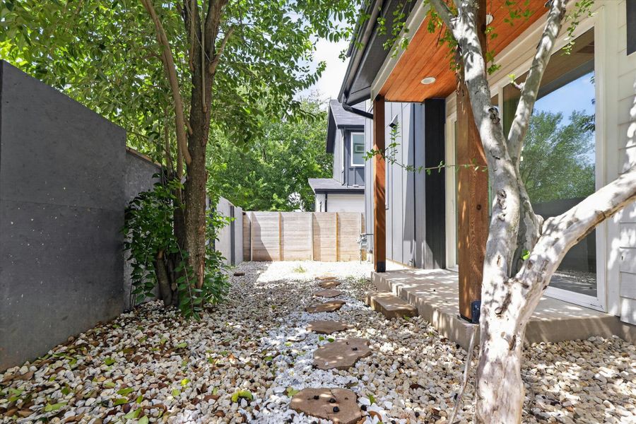 A tranquil gravel path with stepping stones leads to the private yard, bordered by mature trees and contemporary fencing.