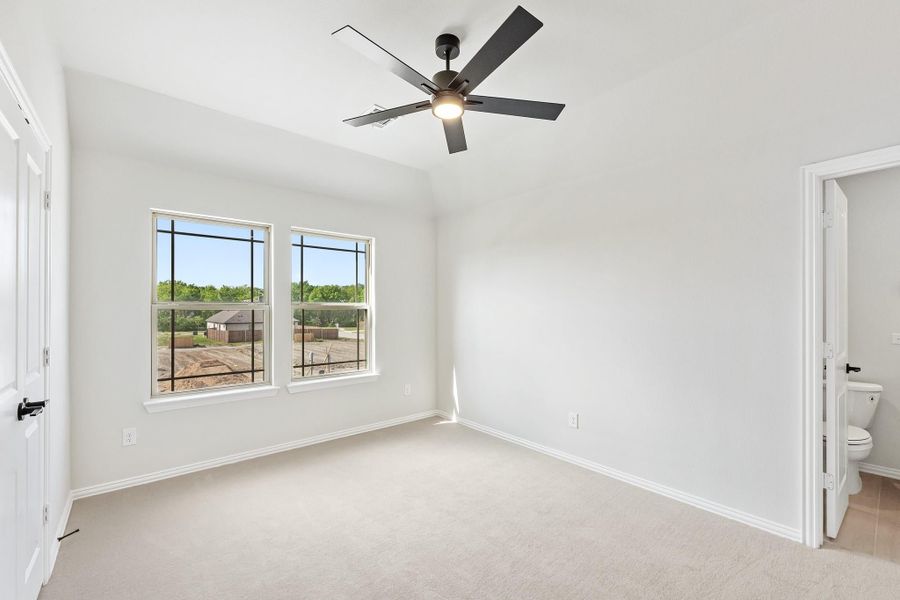 Empty bedroom with carpet, ceiling fan, two windows, and an attached bathroom door visible