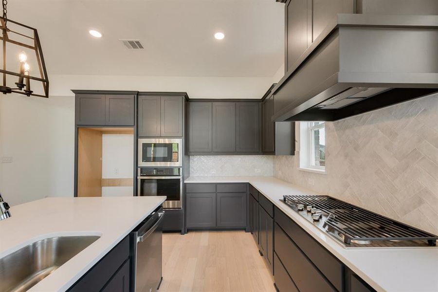 Kitchen with under cabinet range hood, tasteful backsplash, appliances with stainless steel finishes, light wood-style floors, and recessed lighting Kitchen with under cabinet range hood, tasteful backsplash, appliances with stainless steel finishes, light wood-style floors, and recessed lighting
