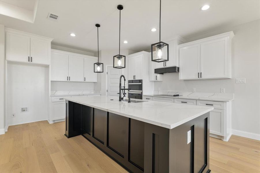 Kitchen with visible vents, hanging light fixtures, a kitchen island with sink, white cabinets, and under cabinet range hood