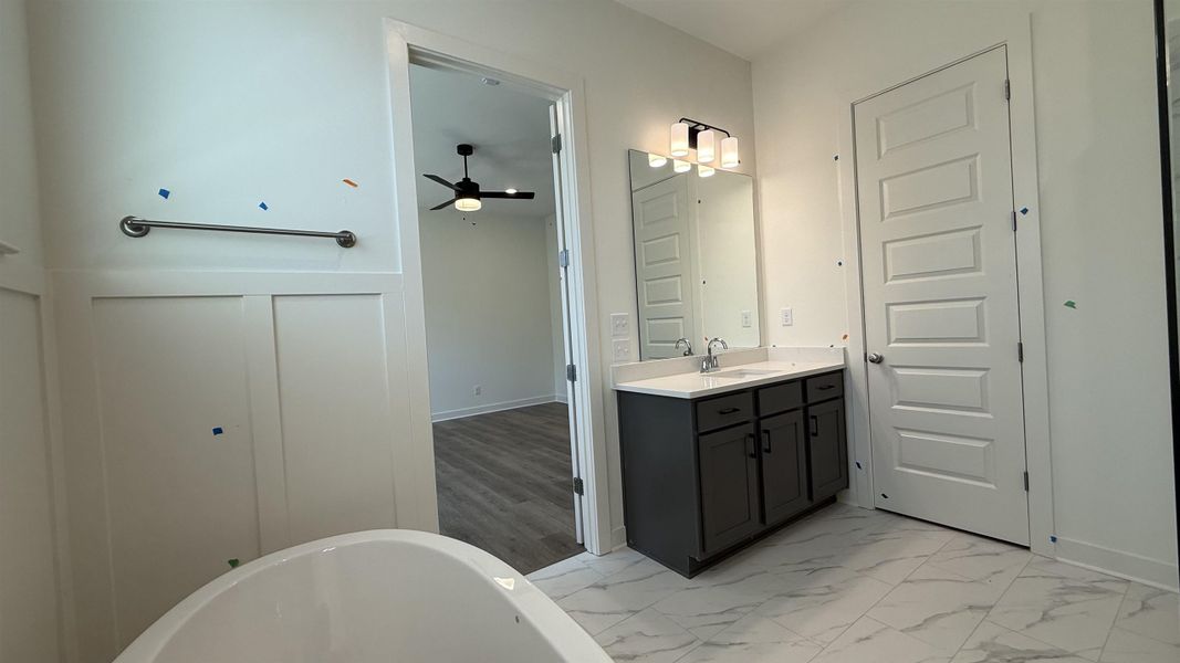 Full bathroom with a soaking tub, vanity, light marble finish floors, and ceiling fan