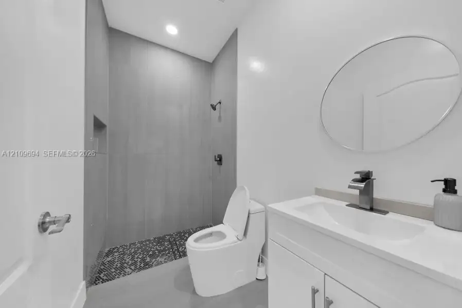 Bathroom featuring a walk-in shower with vertical tile surround and mosaic tile flooring, a modern vanity with integrated sink, a single-handle faucet, and an oval wall-mounted mirror