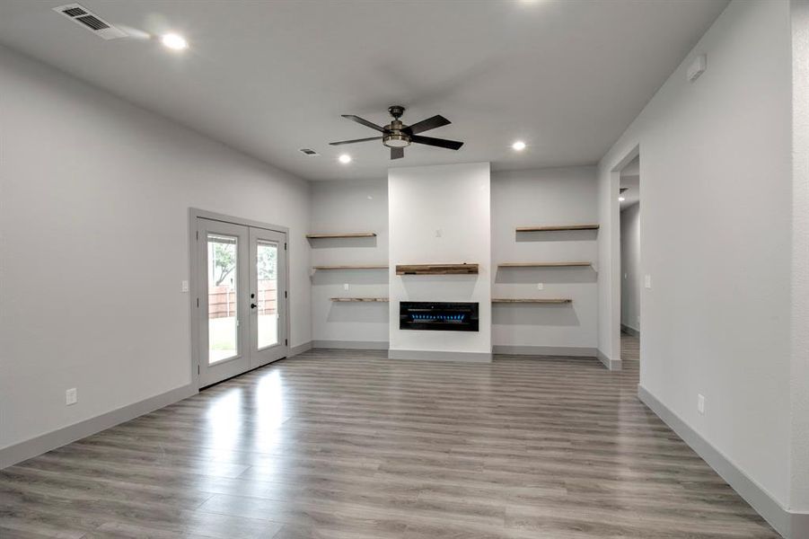 Unfurnished living room with french doors, light wood finished floors, ceiling fan, recessed lighting, and a glass covered fireplace Unfurnished living room with french doors, light wood finished floors, ceiling fan, recessed lighting, and a glass covered fireplace