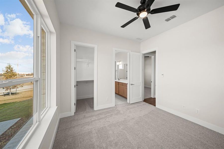 Unfurnished bedroom featuring light carpet, a walk in closet, ceiling fan, and ensuite bath