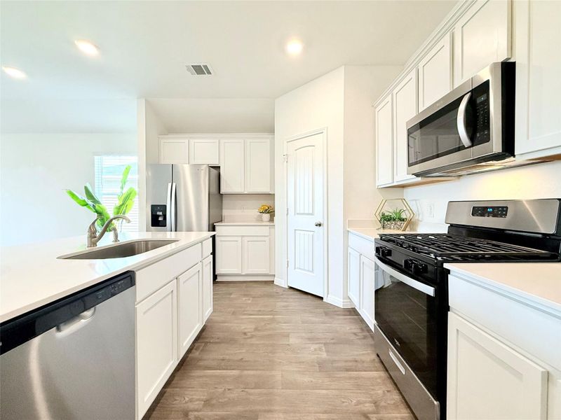 Kitchen featuring stainless steel appliances, white cabinetry, light wood-style flooring, recessed lighting, and light stone counters Kitchen featuring stainless steel appliances, white cabinetry, light wood-style flooring, recessed lighting, and light stone counters
