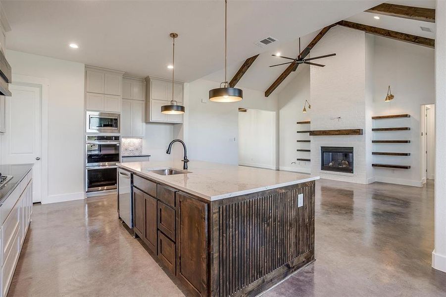 Kitchen with sink, stainless steel appliances, beamed ceiling, pendant lighting, and a kitchen island with sink