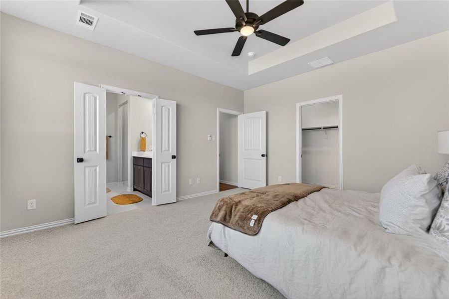 Bedroom with a tray ceiling, light carpet, ceiling fan, and ensuite bath Bedroom with a tray ceiling, light carpet, ceiling fan, and ensuite bath