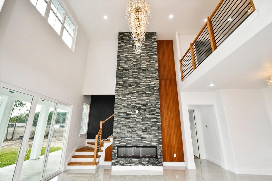 The living room’s striking centerpiece is a floor-to-ceiling stacked stone fireplace with a modern linear insert, flanked by elegant wood-cladding and framed by abundant natural light.