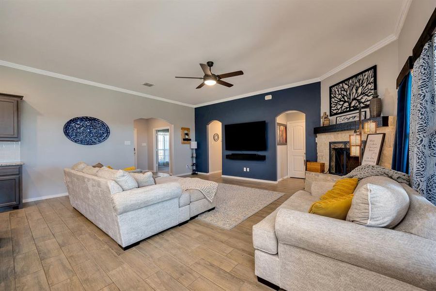 Living area featuring wood finished floors, ceiling fan, crown molding, and arched walkways