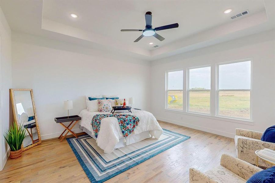 Bedroom featuring light hardwood / wood-style flooring, ceiling fan, and a tray ceiling