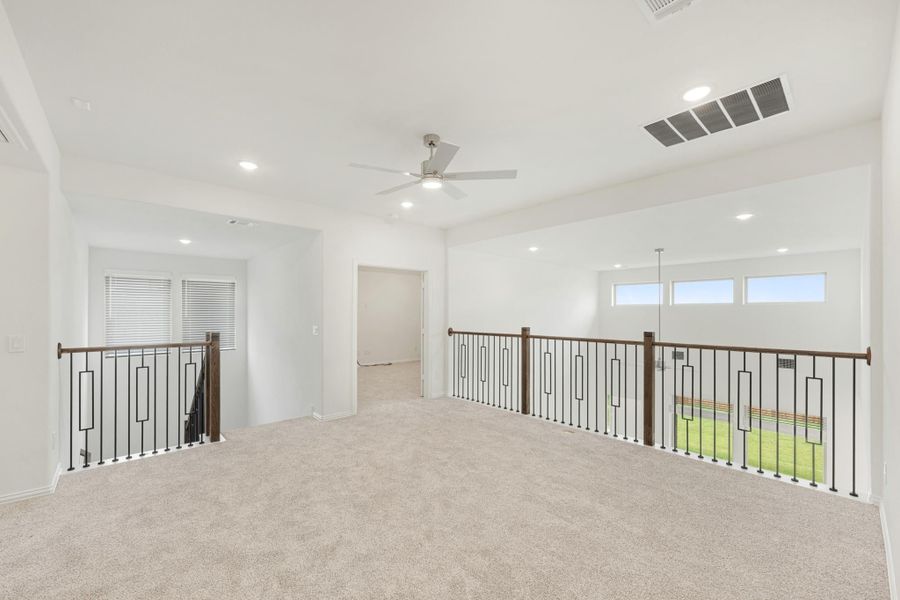 Open upstairs loft with carpet flooring, ceiling fan, and metal railing along staircase opening