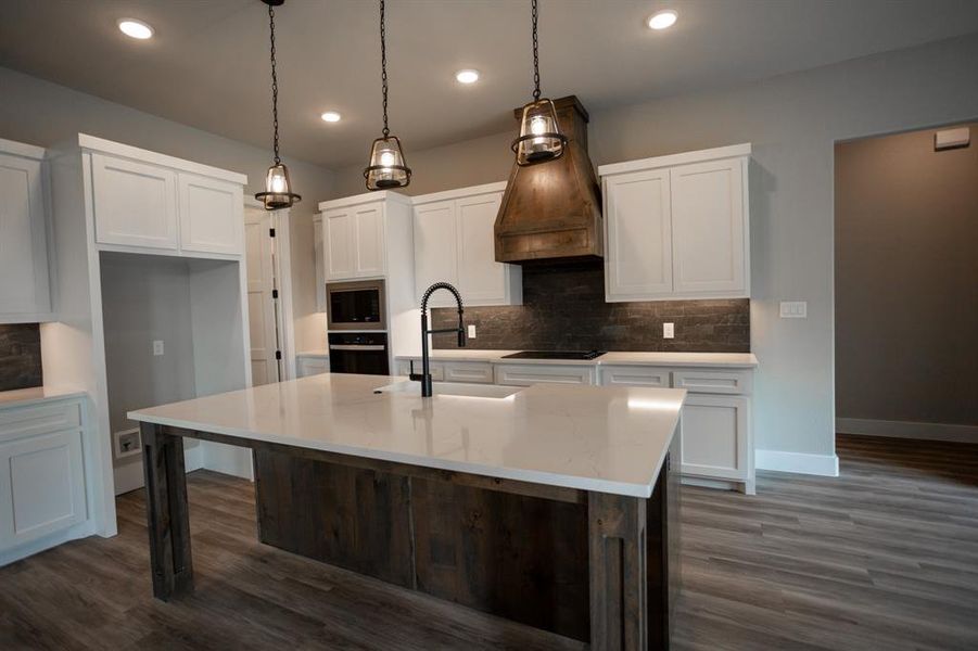 Kitchen with hanging light fixtures, tasteful backsplash, white cabinetry, light stone counters, and dark wood-style flooring Kitchen with hanging light fixtures, tasteful backsplash, white cabinetry, light stone counters, and dark wood-style flooring