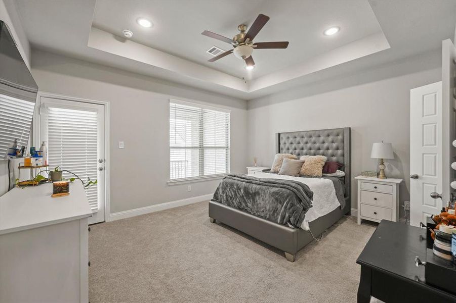 Carpeted bedroom with a tray ceiling and ceiling fan