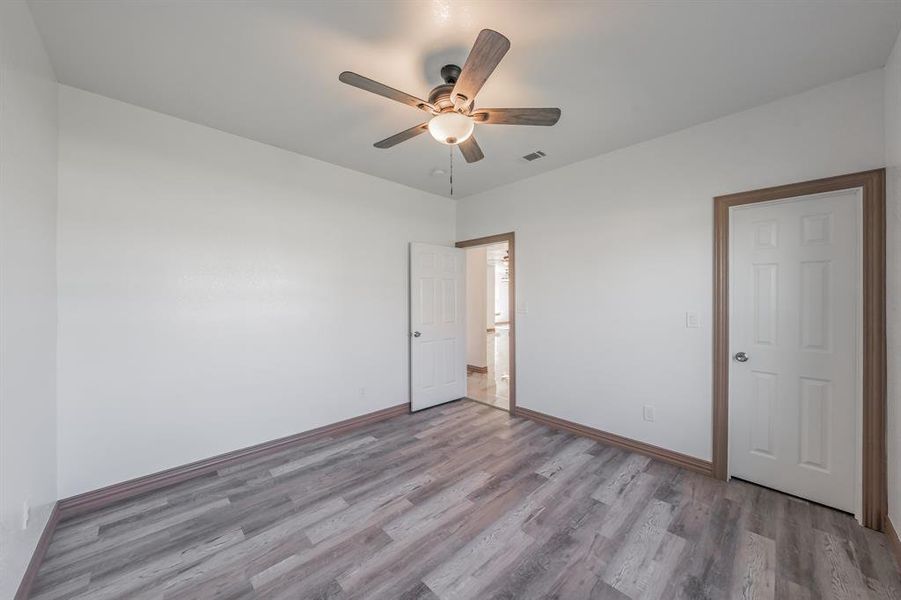 Unfurnished room featuring visible vents, wood finished floors, a ceiling fan, and baseboards