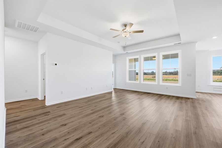 Unfurnished living room with a raised ceiling, light wood-type flooring, and a ceiling fan