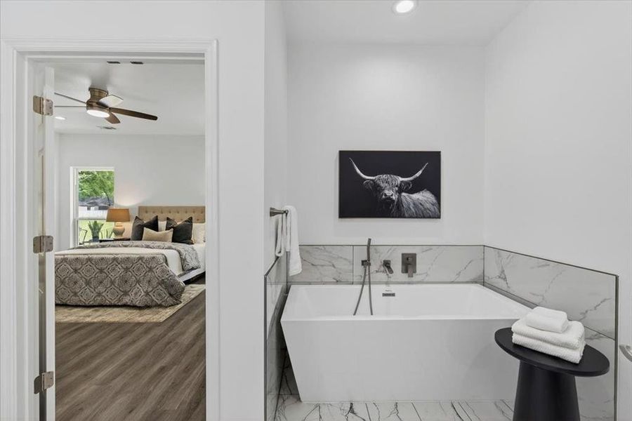 Freestanding soaking tub featuring wall-mounted fixtures and a marble-patterned tile surround