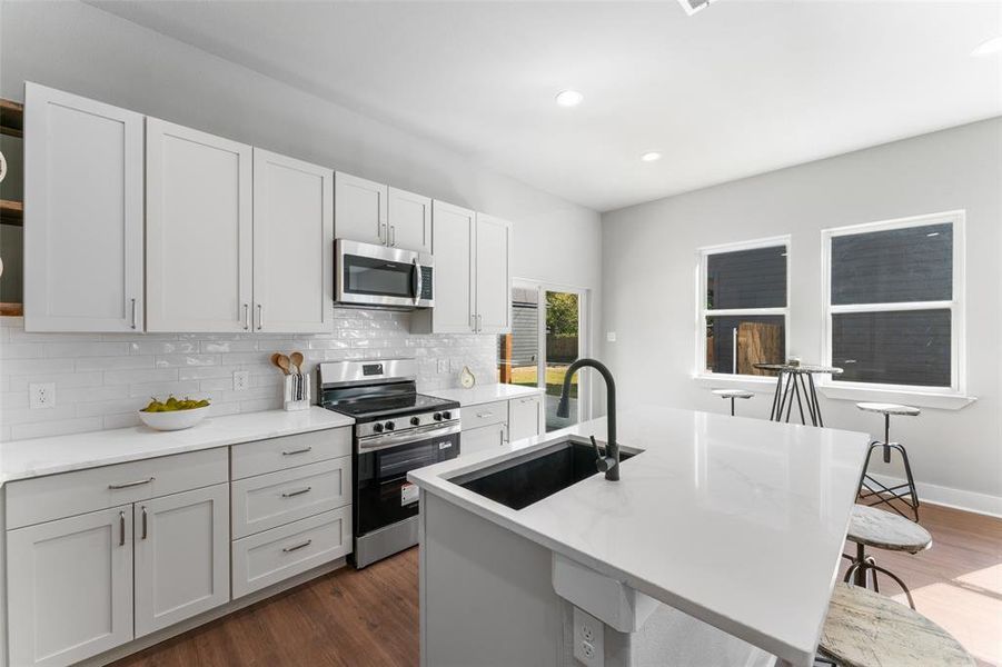 Kitchen featuring stainless steel appliances, decorative backsplash, light stone countertops, a breakfast bar area, and recessed lighting