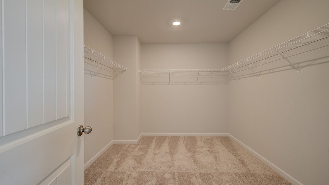 Stonefield primary walk-in closet with two rows of built-in shelving and carpet flooring at Brighton in Locust Grove, GA.