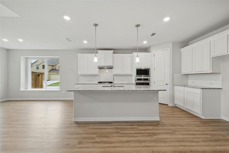 Kitchen featuring stainless steel appliances, under cabinet range hood, light wood finished floors, a sink, and tasteful backsplash Kitchen featuring stainless steel appliances, under cabinet range hood, light wood finished floors, a sink, and tasteful backsplash