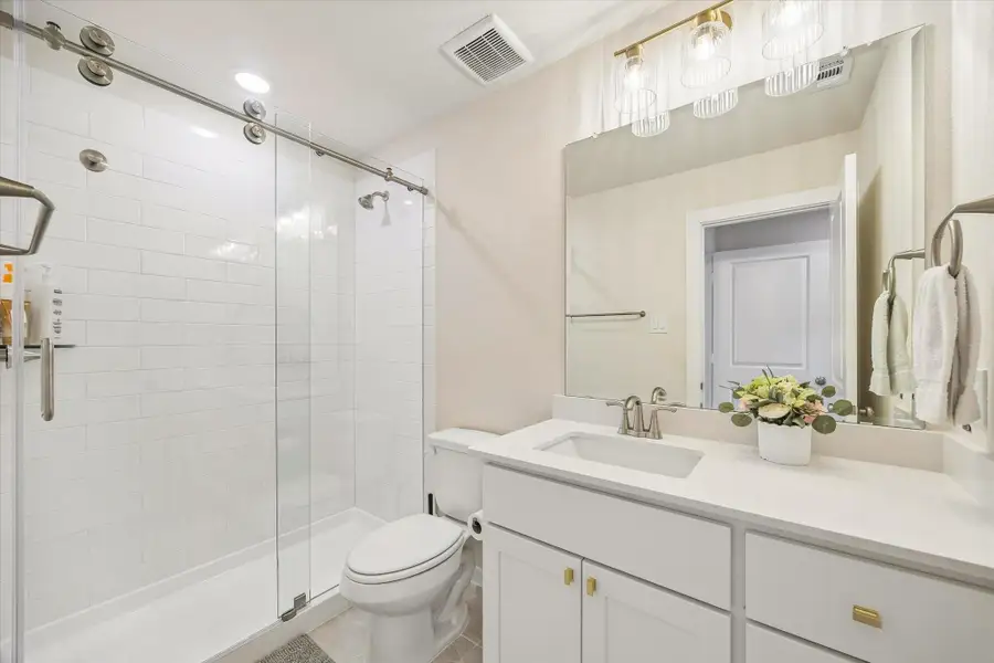 SECONDARY BATH FEATURES A GLASS-ENCLOSED SHOWER, WHITE TILE SURROUND, QUARTZ VANITY, AND MODERN LIGHTING. SECONDARY BATH FEATURES A GLASS-ENCLOSED SHOWER, WHITE TILE SURROUND, QUARTZ VANITY, AND MODERN LIGHTING.