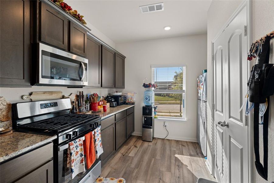 Kitchen featuring stainless steel appliances, dark brown cabinets, light wood-style floors, light stone counters, and recessed lighting