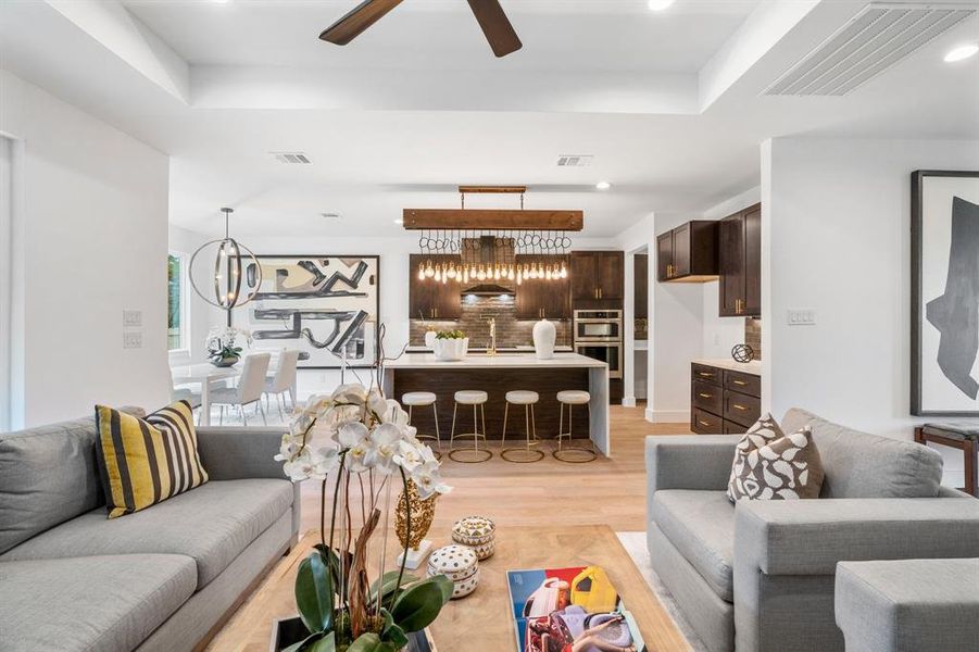 Living room with sink, light wood-type flooring, a raised ceiling, and ceiling fan with notable chandelier