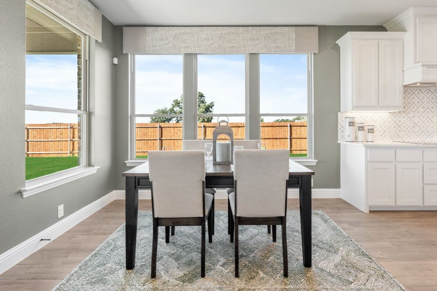 Dining area with dark wood table, white upholstered chairs, large windows, and hardwood floors adjacent to kitchen