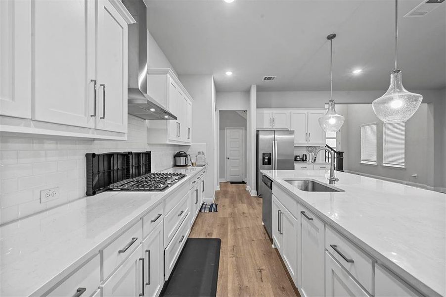 Kitchen with white cabinetry, light stone counters, decorative light fixtures, light wood floors, and backsplash
