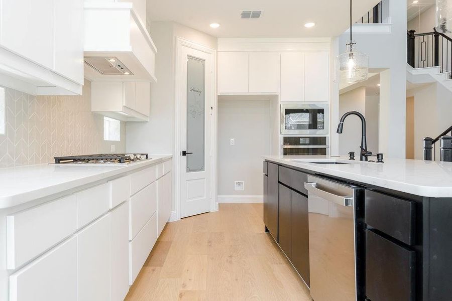 Kitchen featuring appliances with stainless steel finishes, white cabinetry, pendant lighting, and light wood-type flooring