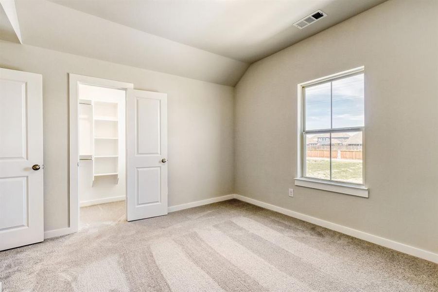 Unfurnished bedroom with light carpet, a spacious closet, and vaulted ceiling