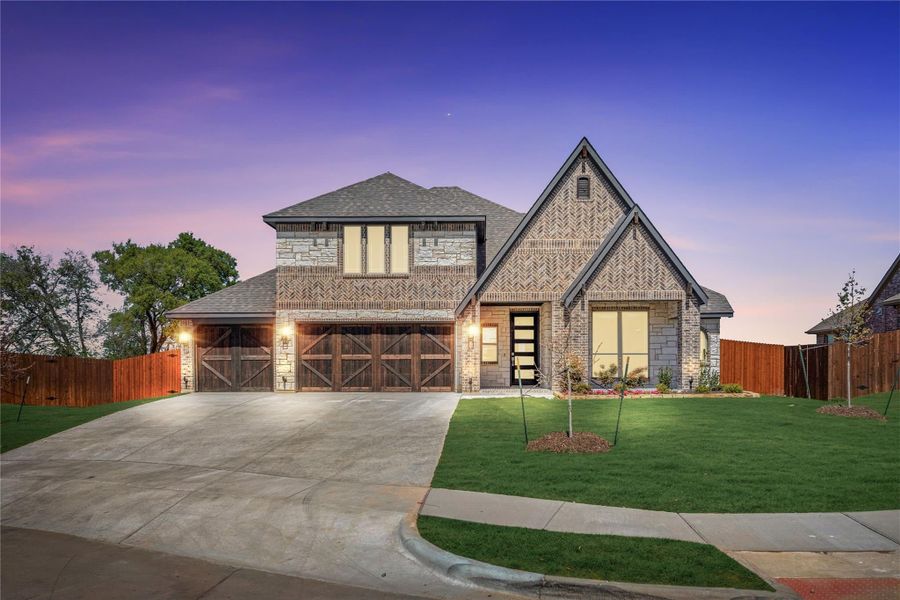 Two-story brick home with three-car garage, wood doors, and manicured front lawn at dusk