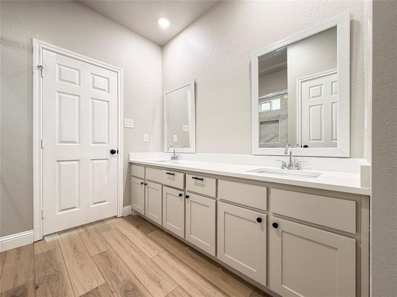 Bathroom featuring double vanity, light wood-type flooring, a textured wall, and a shower Bathroom featuring double vanity, light wood-type flooring, a textured wall, and a shower