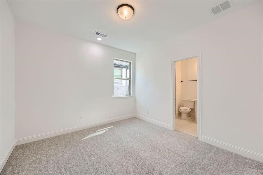 Carpeted room with a single window, recessed lighting, ceiling light fixture, and an attached bathroom featuring a toilet and towel rack Carpeted room with a single window, recessed lighting, ceiling light fixture, and an attached bathroom featuring a toilet and towel rack