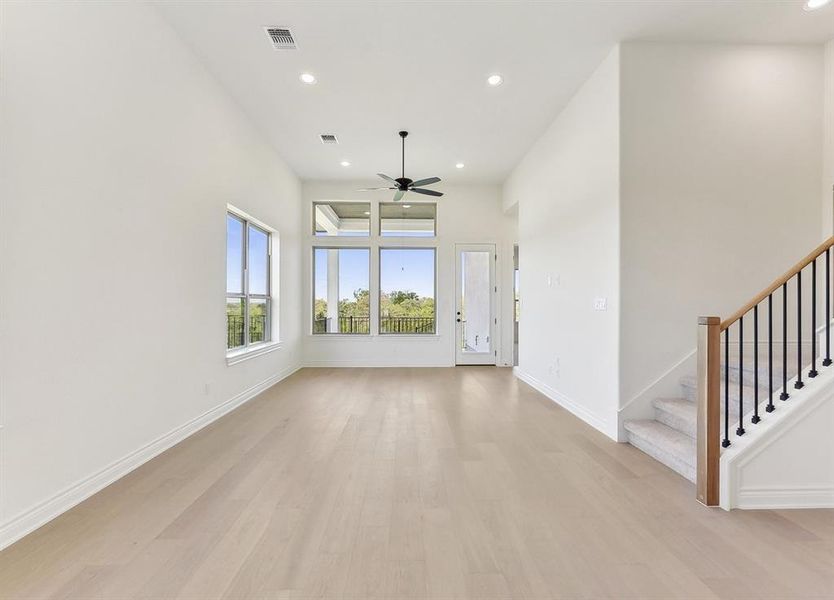 Spacious living area featuring light-toned wood floors, high ceilings with recessed lighting, and a ceiling fan